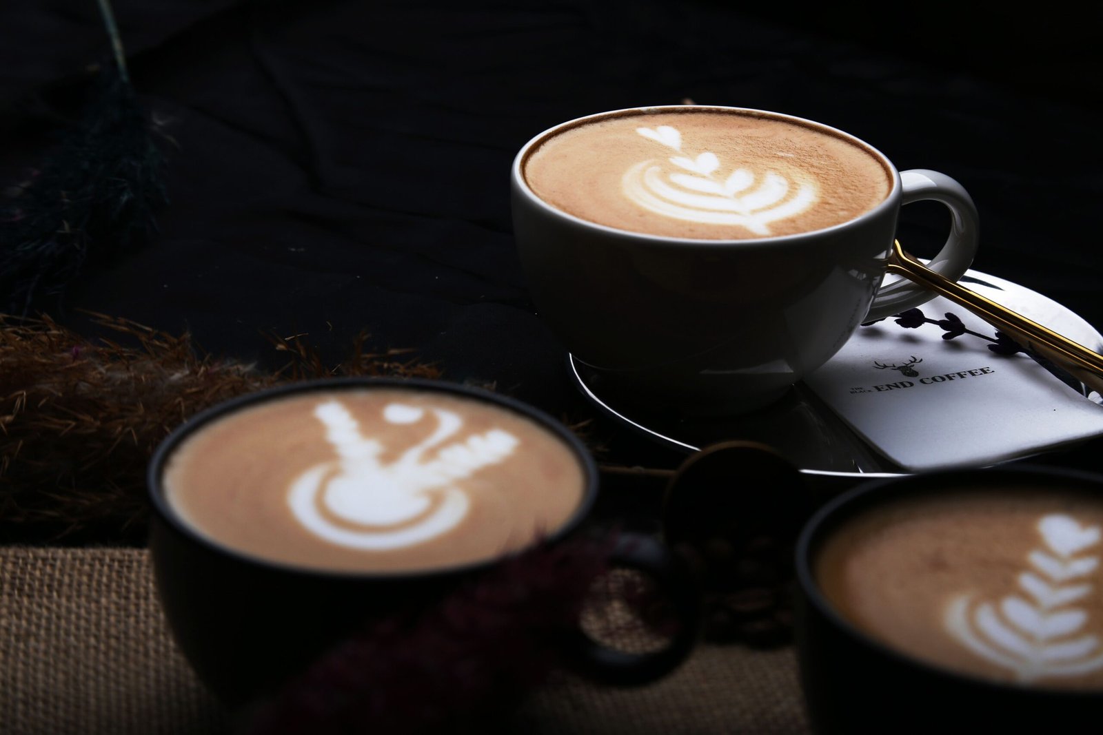 Close-up of beautifully crafted latte art in three cups of coffee, showcasing intricate designs.